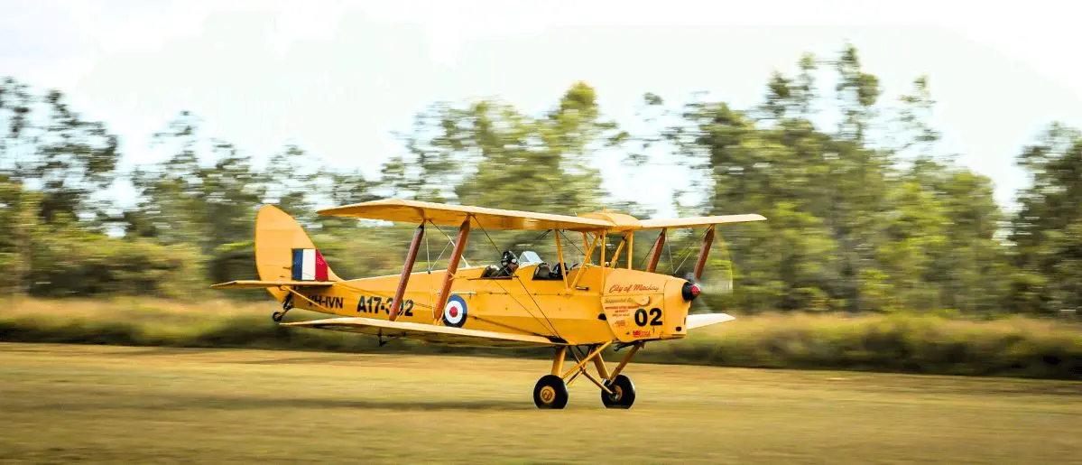The 'City of Mackay' Tiger Moth, marked A17-302, with two pilots in the open cockpit, accelerating on a grassy airstrip The 'City of Mackay' Tiger Moth, marked A17-302, with two pilots in the open cockpit, accelerating on a grassy airstrip