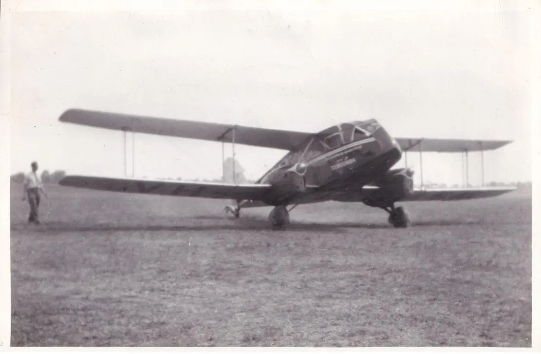 De Havilland Dragon VH-ABK “City of Toowoomba”. If you look closely there appears to be a dog chasing the tailwheel of the aircraft.