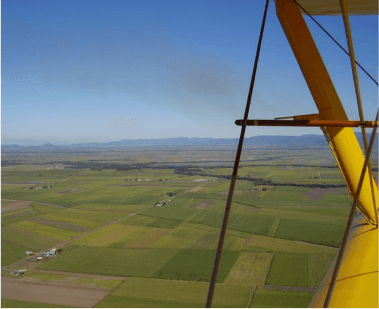 A scenic view of vast green farmland and rolling hills from the cockpit of a Tiger Moth biplane, showcasing the beauty of the Mackay region A scenic view of vast green farmland and rolling hills from the cockpit of a Tiger Moth biplane, showcasing the beauty of the Mackay region