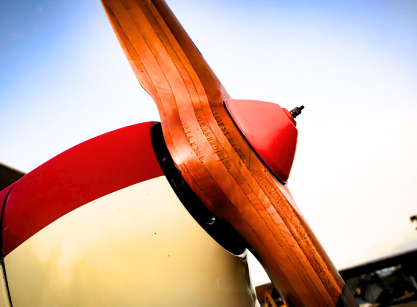 A detailed view of a vintage wooden aircraft propeller with a red spinner, highlighting craftsmanship and classic aviation engineering. A detailed view of a vintage wooden aircraft propeller with a red spinner, highlighting craftsmanship and classic aviation engineering.