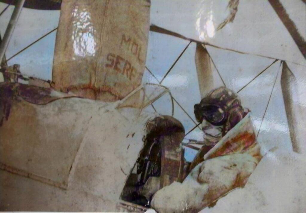 Mechanics repairing a Tiger Moth aircraft engine in the field using a tripod hoist, with a vintage spray service truck nearby, during its use in aerial agriculture.
