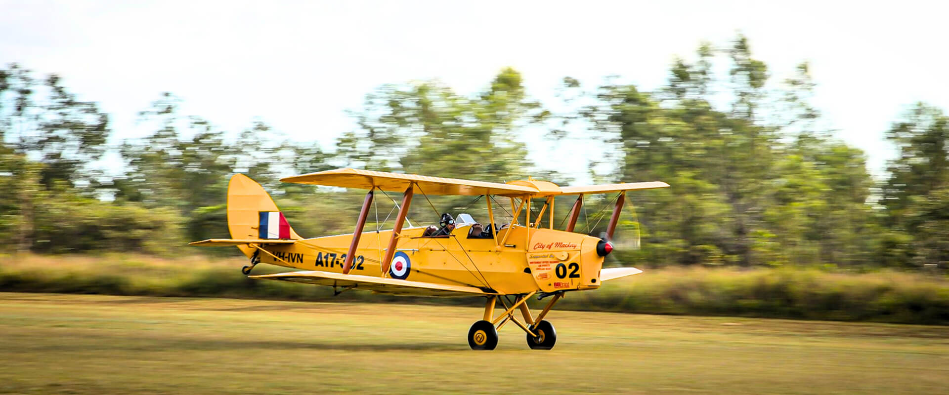 The 'City of Mackay' Tiger Moth, marked A17-302, with two pilots in the open cockpit, accelerating on a grassy airstrip