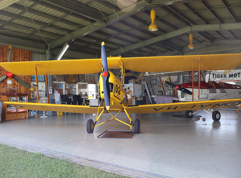 A vintage yellow Tiger Moth biplane, 'City of Mackay' (A17-302), with two pilots in the open cockpit, sits on a grassy airfield. Preserved by the Mackay Tiger Moth Museum. A vintage yellow Tiger Moth biplane, 'City of Mackay' (A17-302), with two pilots in the open cockpit, sits on a grassy airfield. Preserved by the Mackay Tiger Moth Museum.